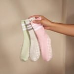Hand holding three pastel Pilates grip socks with non-slip sole grips.