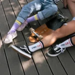 Custom white GYMNA CLUB crew socks worn with black skate shoes beside a skateboard.