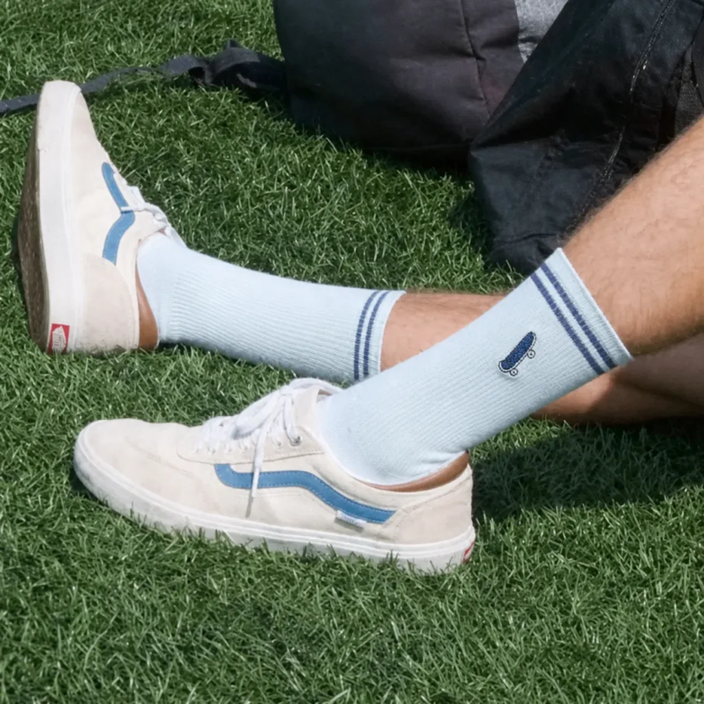 Light blue custom embroidered crew socks with a skateboard logo worn outdoors.