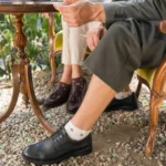Custom floral ankle dress socks worn with leather dress shoes at an outdoor coffee table.