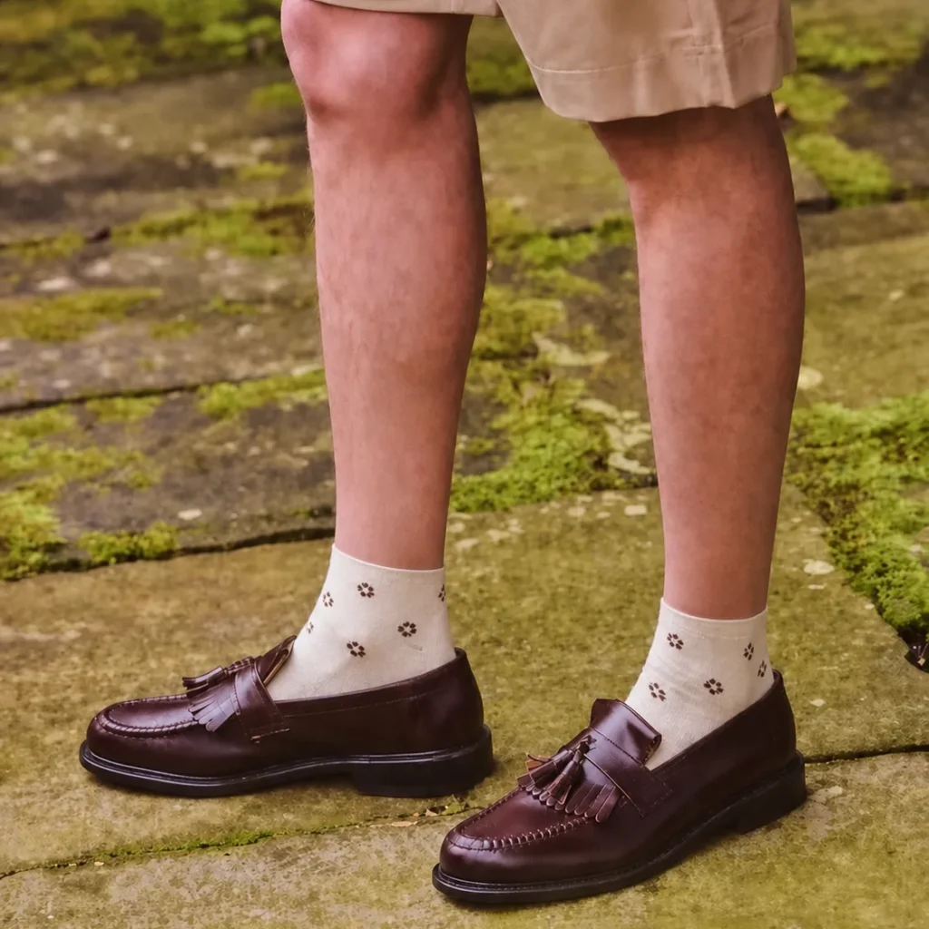 Cream custom ankle dress socks with small brown floral patterns worn with brown leather loafers.