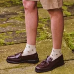 Cream custom ankle dress socks with small brown floral patterns worn with brown leather loafers.