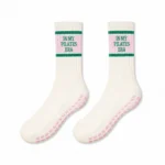 Pair of cream Pilates grip socks with pink text panels, green stripes, and pink silicone grips on a white background.