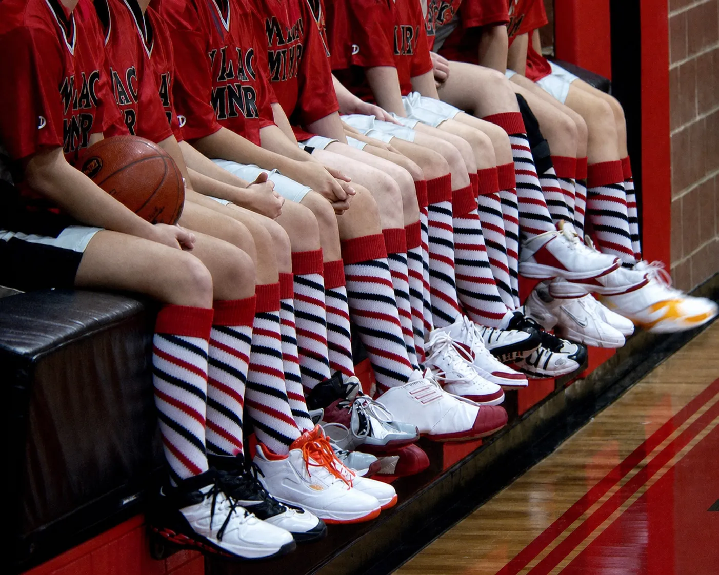 Basketball team players wearing custom red, white, and navy over the calf athletic socks on the bench.