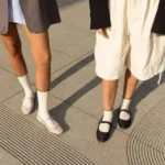 Women wearing white custom ruffle socks with black scalloped cuffs and Mary Jane shoes.
