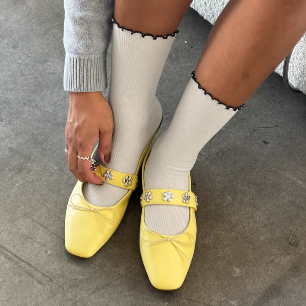 Cream custom ruffle socks with black scalloped cuffs worn with yellow Mary Jane shoes.