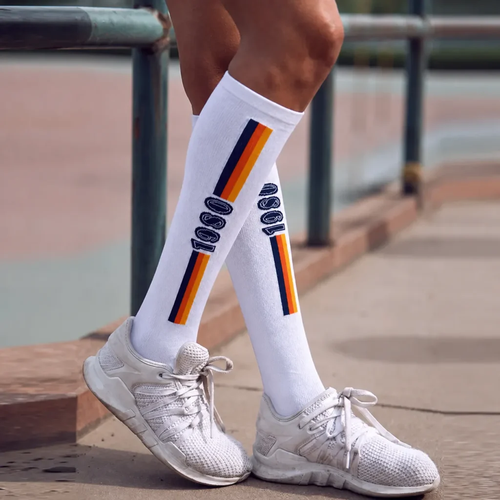 Athlete wearing white custom knee high athletic socks with navy orange and yellow stripes