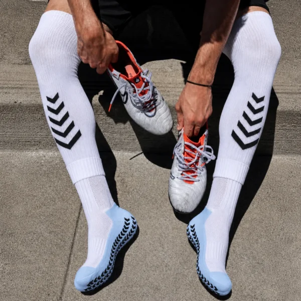 Athlete putting on white soccer grip socks with light blue foot panels and black anti-slip pads.